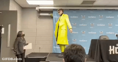 A Man In A Yellow Suit Is Standing On A Stage In Front Of A Crowd . GIF