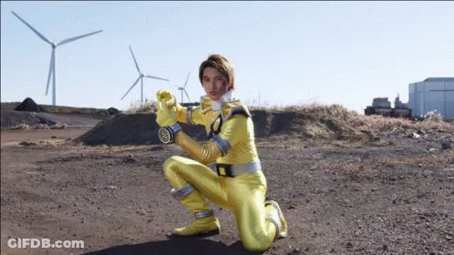 A Man In A Yellow Superhero Costume Is Kneeling In A Dirt Field GIF
