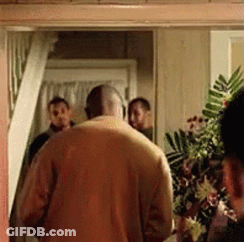 A Man In A Yellow Sweater Is Standing In A Doorway With A Group Of People Behind Him . GIF
