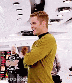 A Man In A Yellow Sweater Is Standing In A Room With His Arms Crossed . GIF