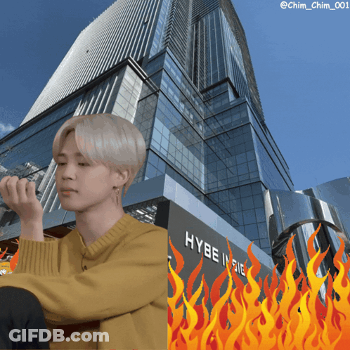 A Man In A Yellow Sweater Sits In Front Of A Building That Says Hybe Indie GIF