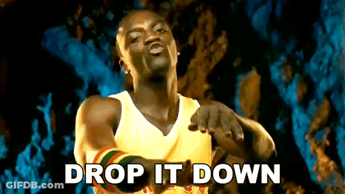A Man In A Yellow Tank Top Is Pointing At The Camera With The Words Drop It Down Written Below Him GIF