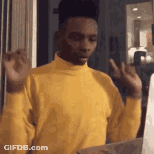 A Man In A Yellow Turtleneck Sweater Is Making A Funny Face While Holding A Box . GIF