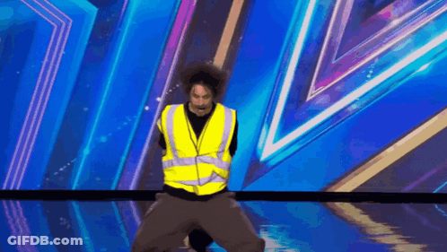 A Man In A Yellow Vest Is Standing On A Stage GIF