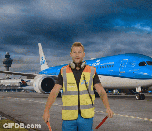 A Man In A Yellow Vest Stands In Front Of A Blue Klm Plane GIF