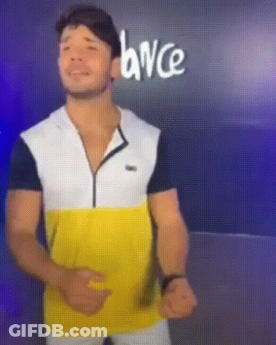 A Man In A Yellow White And Black Shirt Is Dancing In Front Of A Sign That Says Dance GIF