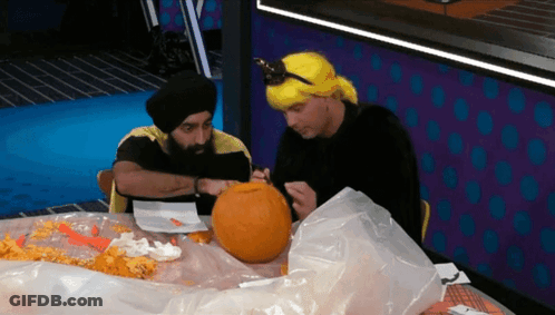 A Man In A Yellow Wig Is Carving A Pumpkin With Another Man GIF