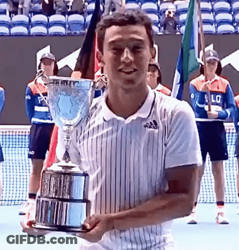 A Man In An Adidas Shirt Is Holding A Trophy On A Tennis Court GIF