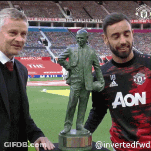 A Man In An Aon Jersey Stands Next To A Man Holding A Statue GIF
