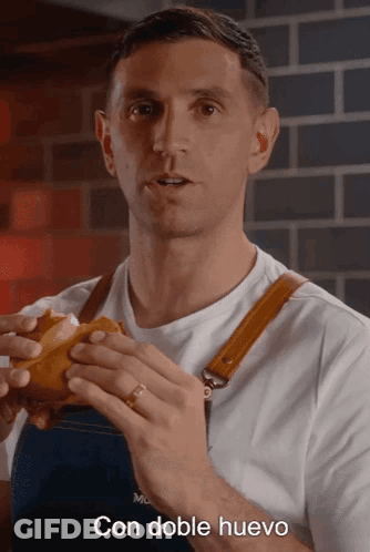 A Man In An Apron Is Holding A Sandwich With The Words Con Doble Huevo Written Below Him GIF