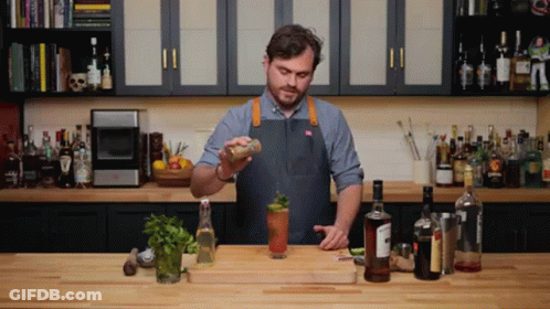 A Man In An Apron Is Preparing A Drink In A Kitchen With Many Bottles GIF