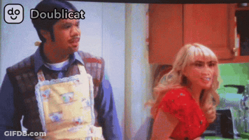 A Man In An Apron Is Standing Next To A Woman In A Red Shirt And The Words Doublicat Are Above Them GIF