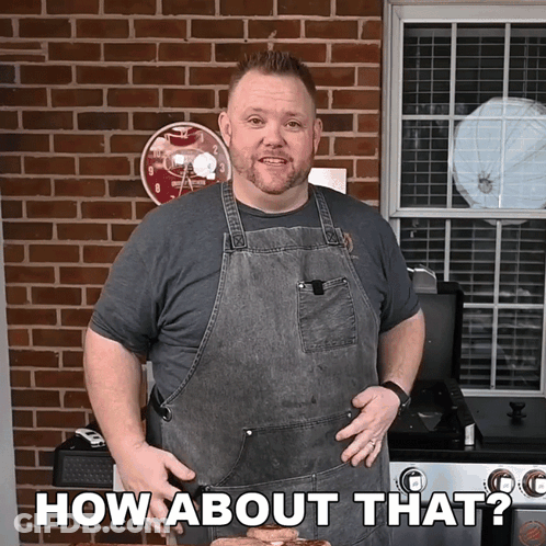 A Man In An Apron Says How About That In Front Of A Brick Wall GIF