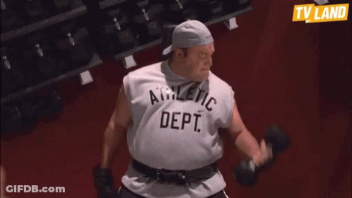 A Man In An Athletic Dept Shirt Is Lifting Dumbbells In A Gym GIF
