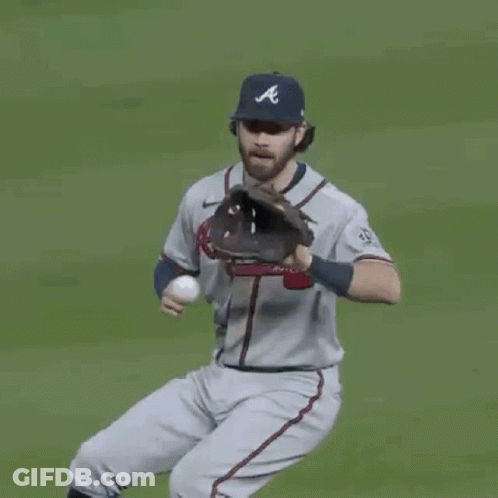 A Man In An Atlanta Braves Jersey Is Standing On A Baseball Field And Smiling . GIF