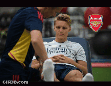 A Man In An Emirates Shirt Sits On A Bed GIF
