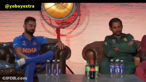 A Man In An India Jersey Sits On A Couch Next To A Man In A Green Uniform GIF