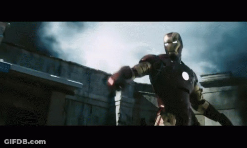 A Man In An Iron Man Suit Is Standing In Front Of A Building With Smoke Coming Out Of It GIF