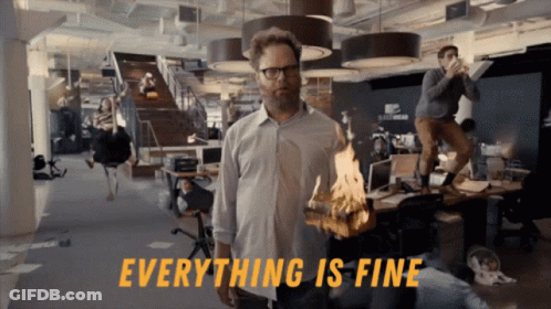 A Man In An Office Holding A Burning Piece Of Wood With The Words Everything Is Fine Behind Him GIF