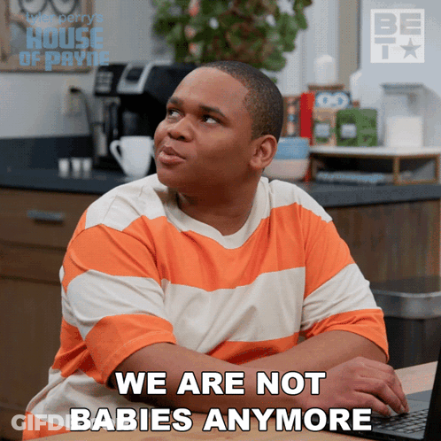 A Man In An Orange And White Striped Shirt Is Sitting In Front Of A Laptop And Says " We Are Not Babies Anymore " GIF