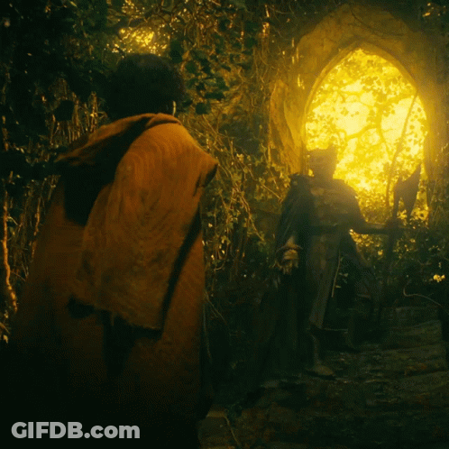 A Man In An Orange Cape Stands In Front Of A Statue In A Dark Forest GIF