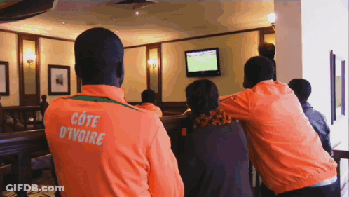 A Man In An Orange Cote D' Ivoire Jacket Watches A Game GIF