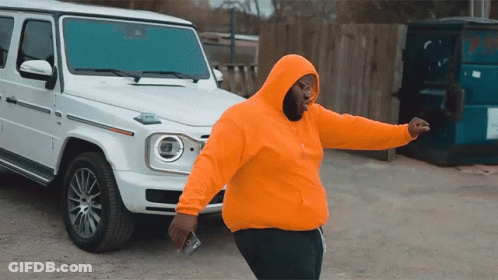 A Man In An Orange Hoodie Is Standing In Front Of A White Jeep GIF