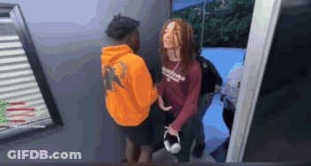 A Man In An Orange Hoodie Is Standing Next To A Woman In A Red Shirt With The Word Supreme On It GIF