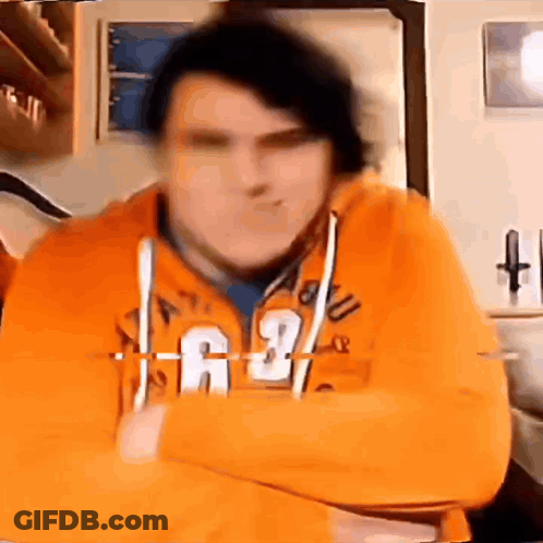 A Man In An Orange Hoodie Is Standing With His Arms Crossed . GIF