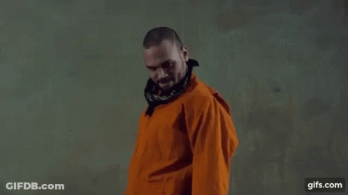 A Man In An Orange Jacket And Bandana Is Standing In Front Of A Wall . GIF