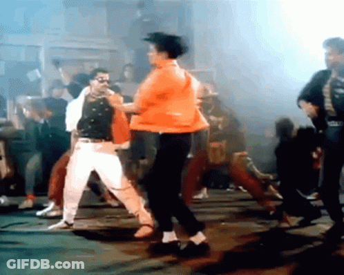 A Man In An Orange Jacket Is Dancing In Front Of A Crowd GIF