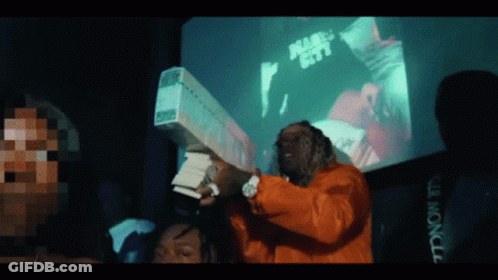 A Man In An Orange Jacket Is Holding A Large Stack Of Money In Front Of A Screen That Says Miami City GIF