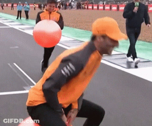 A Man In An Orange Jacket Is Holding An Orange Ball On A Track GIF