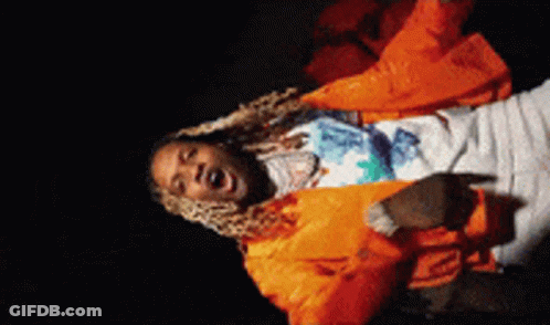 A Man In An Orange Jacket Is Singing Into A Microphone In A Dark Room . GIF