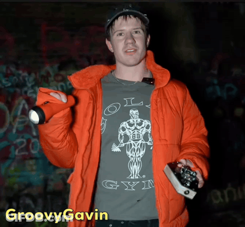 A Man In An Orange Jacket Is Wearing A Shirt That Says Old Gym On It GIF
