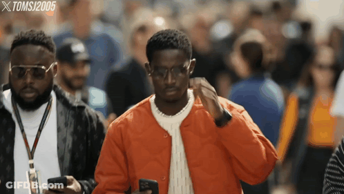 A Man In An Orange Jacket Looks At His Phone While Another Man Looks On GIF