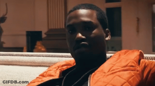 A Man In An Orange Jacket Sits On A White Couch GIF
