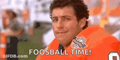 A Man In An Orange Jersey Is Sitting On A Football Field With The Words `` Fooball Time '' Written On His Face . GIF