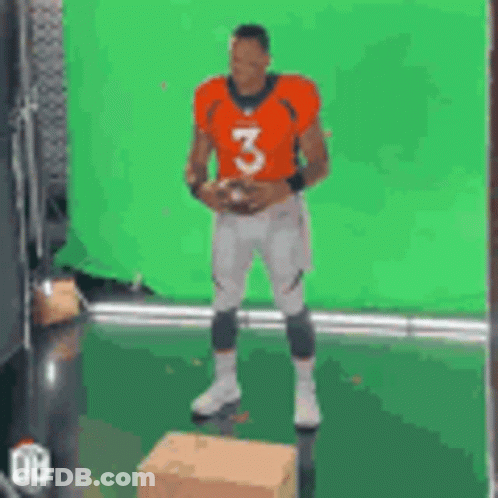 A Man In An Orange Jersey With The Number 3 Is Holding A Football . GIF