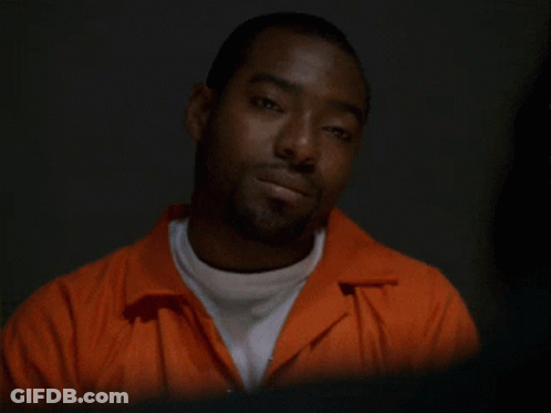 A Man In An Orange Jumpsuit Is Looking Down At Something GIF