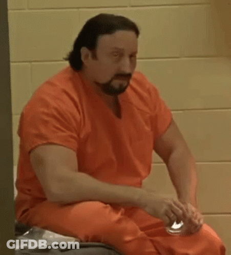 A Man In An Orange Jumpsuit Is Sitting On A Bed In A Prison Cell . GIF
