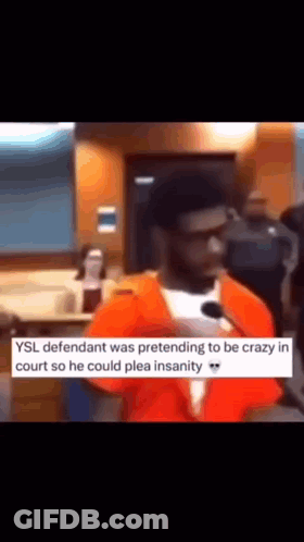 A Man In An Orange Jumpsuit Is Talking Into A Microphone In A Courtroom . GIF