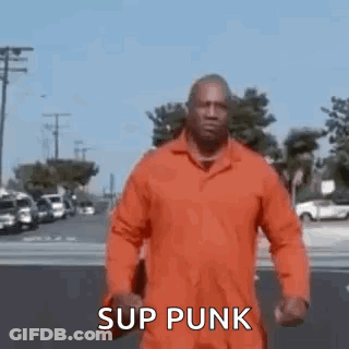 A Man In An Orange Jumpsuit Is Walking Down A Street And Says `` Sup Punk '' . GIF