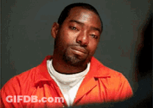 A Man In An Orange Jumpsuit Looks At The Camera With A Serious Look On His Face GIF