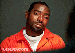 A Man In An Orange Jumpsuit Looks At The Camera With A Serious Look On His Face GIF