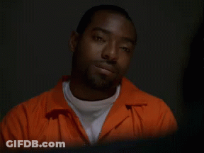 A Man In An Orange Jumpsuit Looks At The Camera With His Eyes Closed GIF