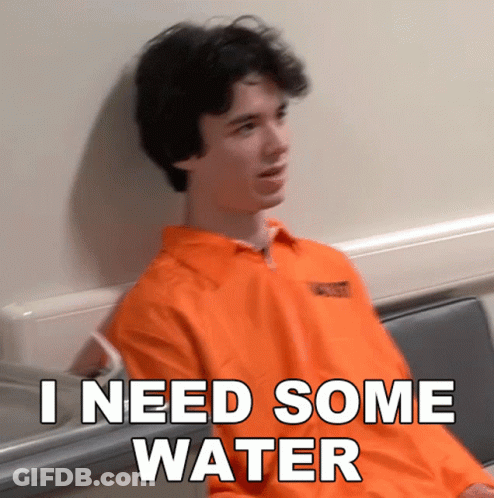 A Man In An Orange Prison Uniform Is Sitting In A Chair And Says I Need Some Water GIF
