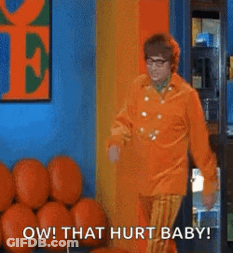 A Man In An Orange Shirt And Striped Pants Is Standing In Front Of A Bunch Of Pumpkins In A Room . GIF