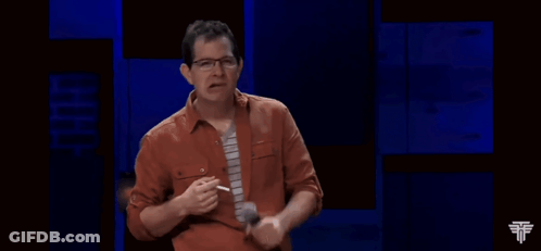 A Man In An Orange Shirt And Tie Is Holding A Microphone In His Hand GIF