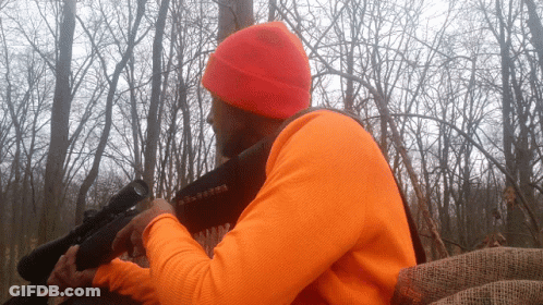 A Man In An Orange Shirt Holds A Rifle GIF
